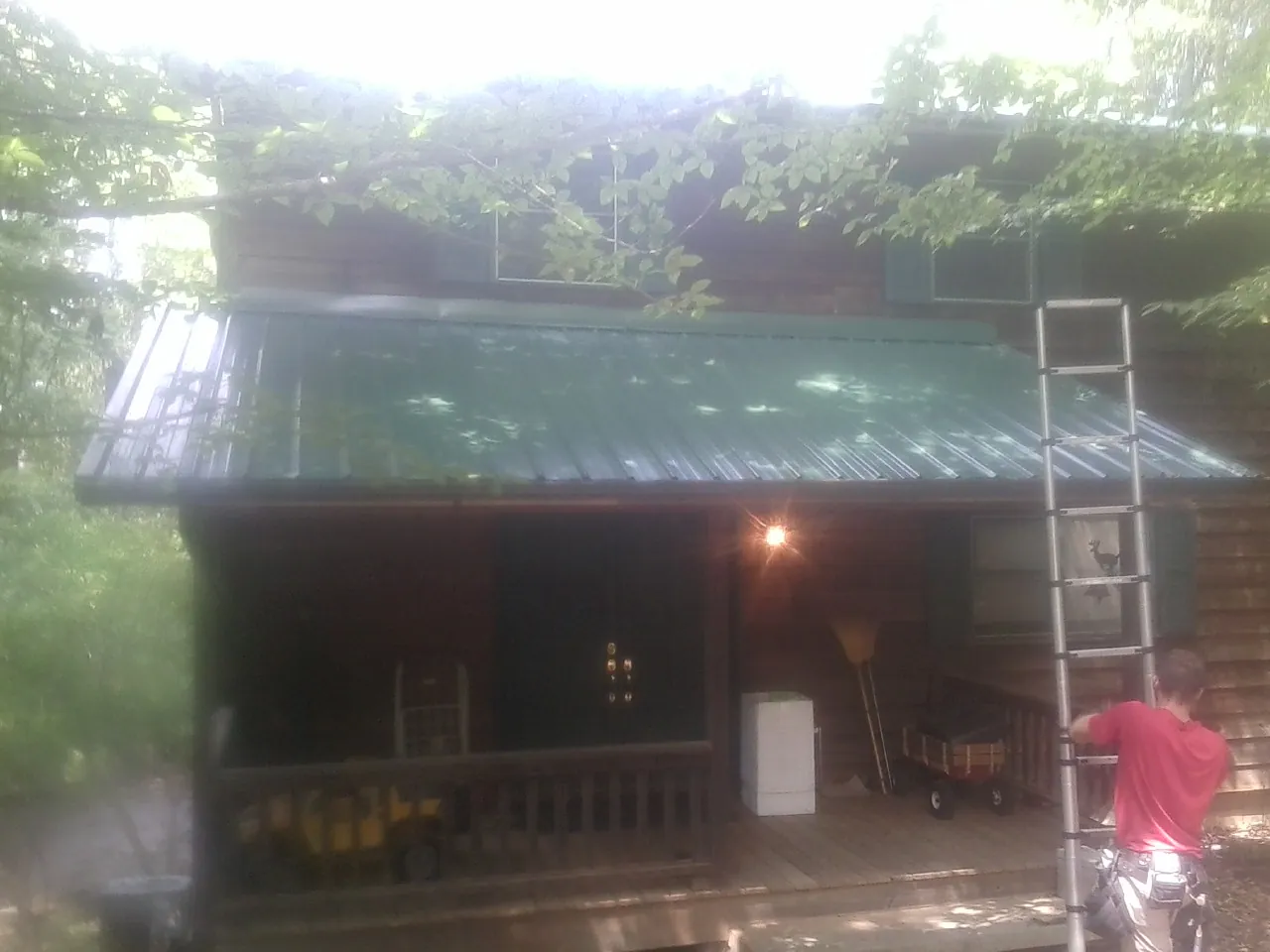 Worker on a ladder at the green porch roof of a wooded cabin in Union City